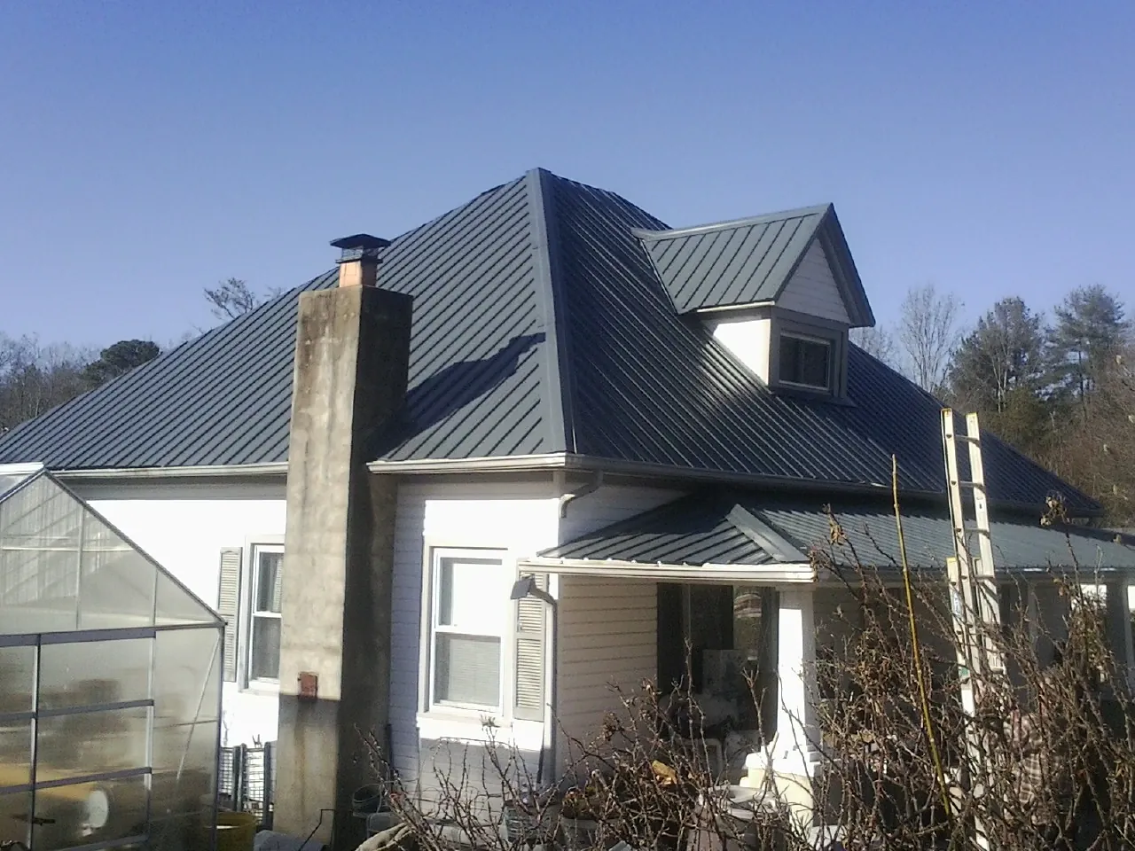 Dark blue standing seam metal roof on a white farmhouse with dormer — Slate & Tile Roof Repair by Roofing Brothers in Llano