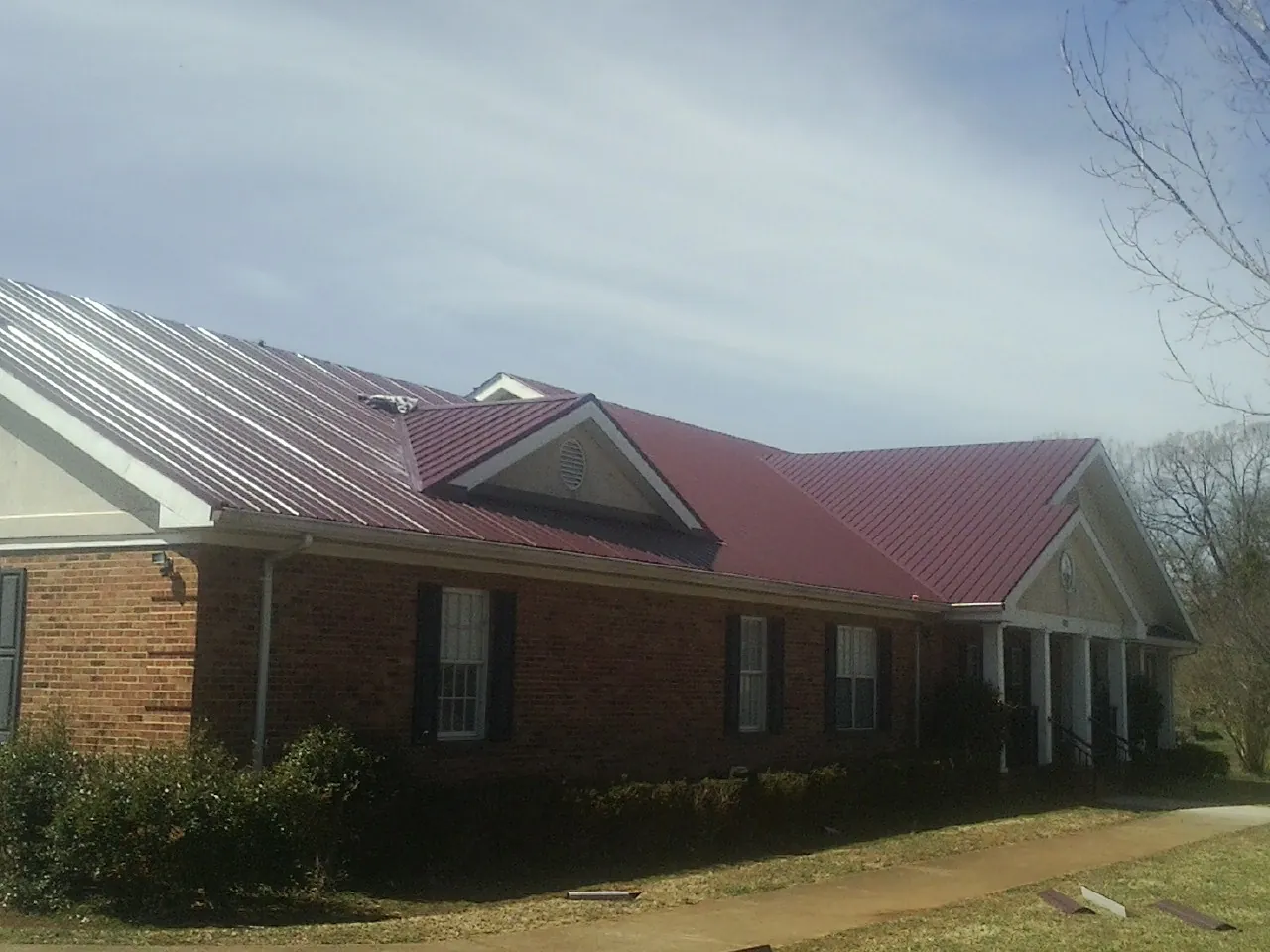 Red metal roof with gabled entries on a long brick building, from a Hail Damage Roof Repair job in Llano