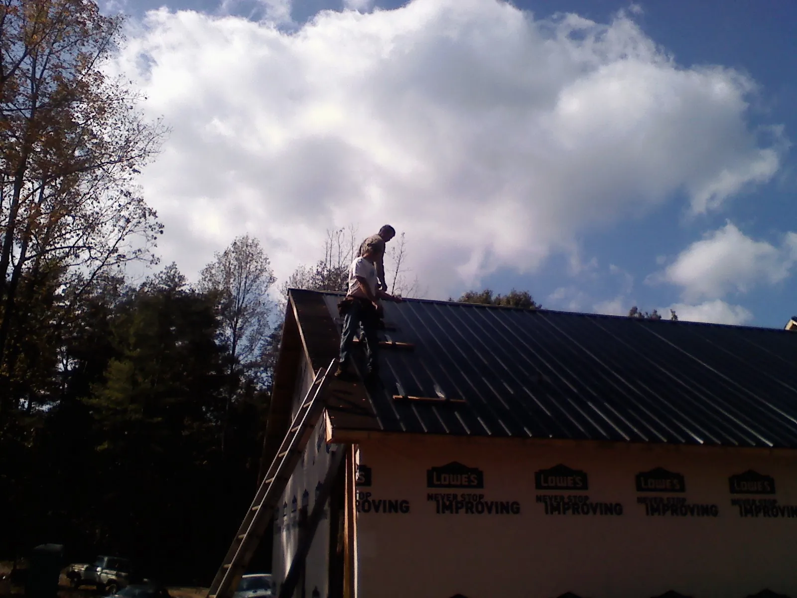 Roofer fastening dark metal panels high against a cloudy sky, from a Roof Inspection job in Llano