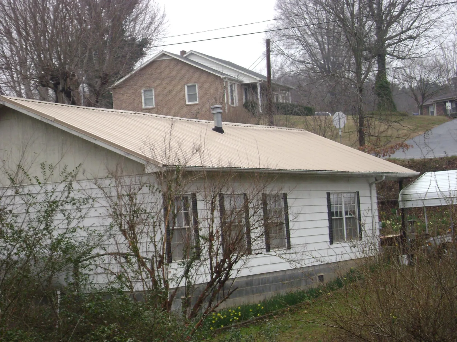 Tan metal roof on a white sided house set into a hillside — Commercial Roofing by Roofing Brothers in Llano